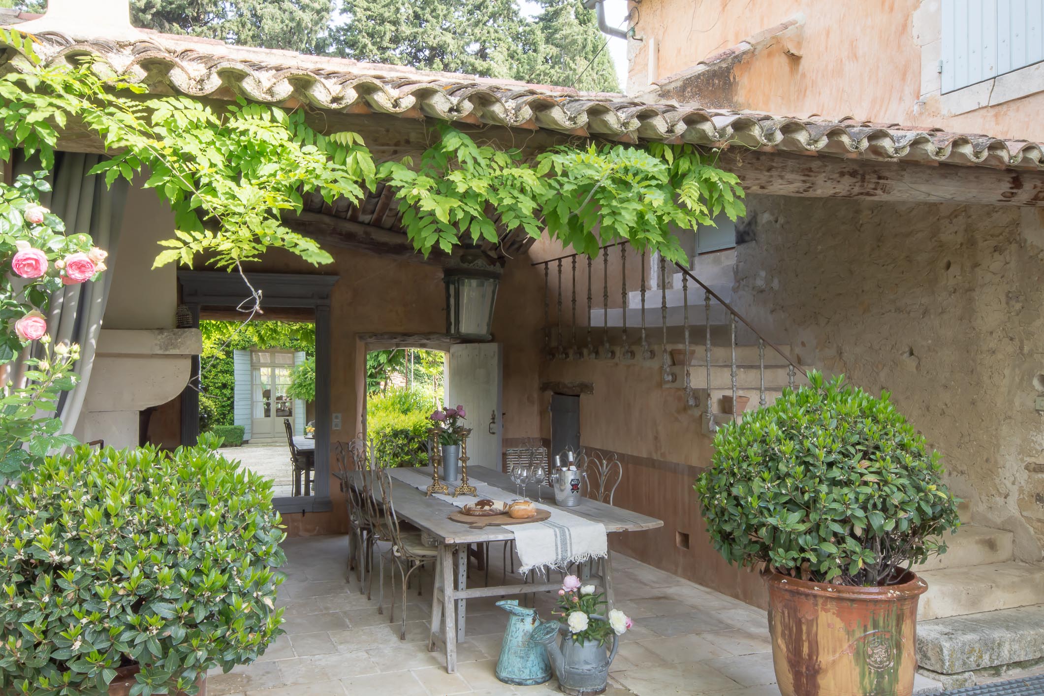 Charming and tranquil French garden scene with beautiful antique Anduze urns as planters lining the garden walls separated by antique concrete columns and outdoor dining seating area