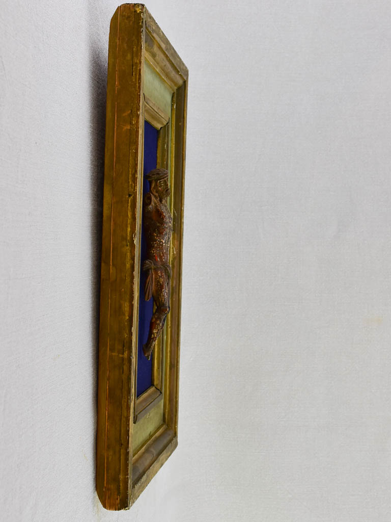 18th Century sculpted wooden Christ on blue fabric with a green and gold frame 11¾" x 18½"